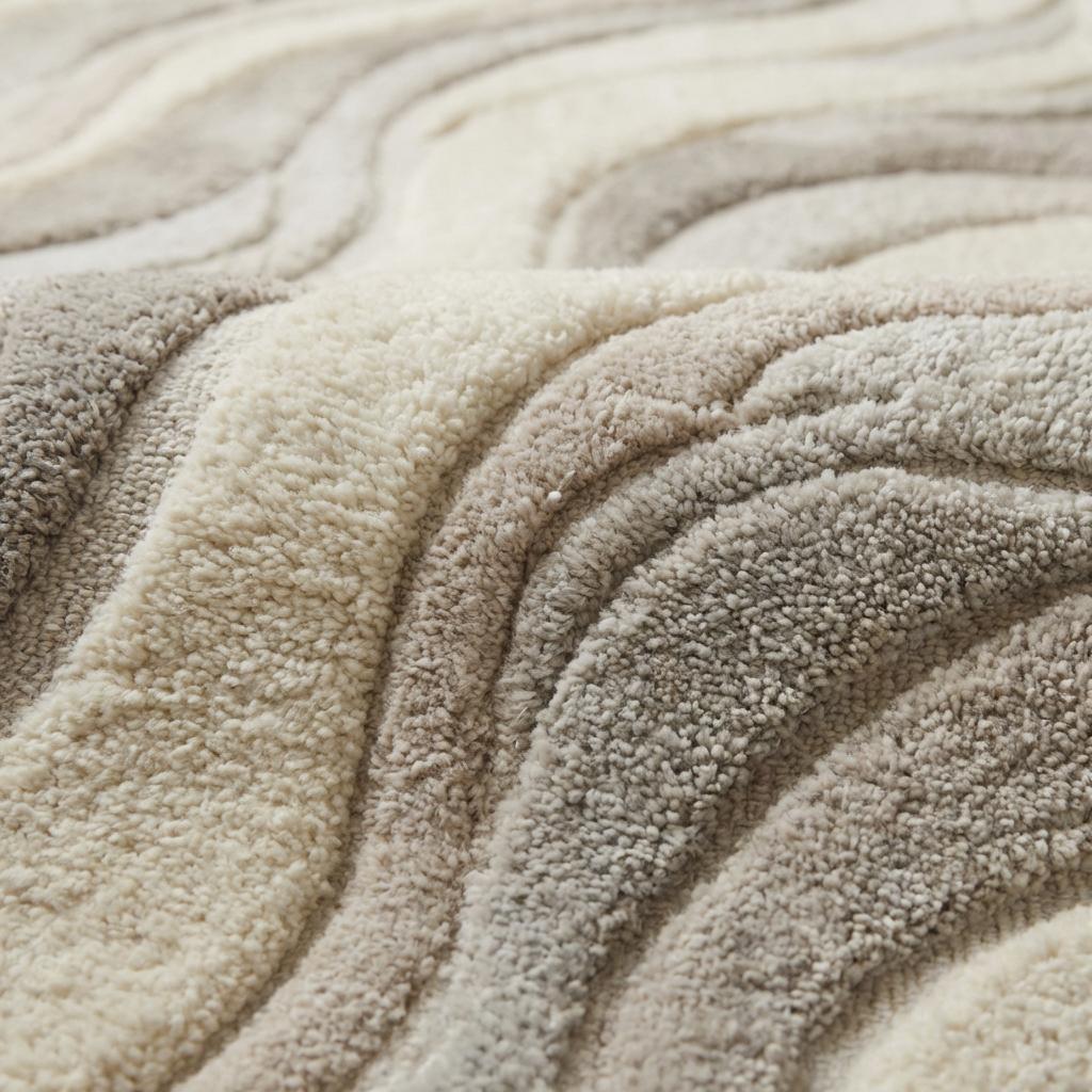 Close-up of carved high-low hand tufted wool pile showing soft dense fibers and sculpted wave texture.