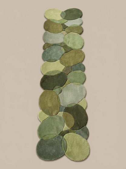 Modern organic runner rug with layered moss and sage green pebble shapes on wood floor