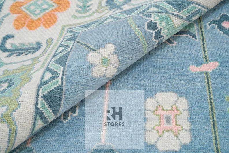 Handmade Oushak wool rug with blue, orange, white floral Turkish knot design in a cozy living room setting