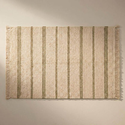 Handwoven wool area rug with chunky knit, green stripes, tassels, and cream base in cozy minimalist interior