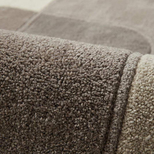 Close-up of plush modern rug fibers showing sculpted high-low pile, soft dense texture, and carved geometric pattern in cream and taupe neutral tones.