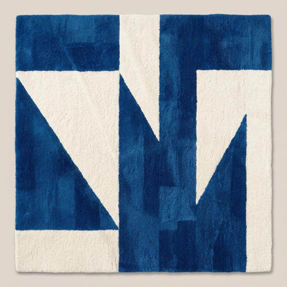 Contemporary blue geometric area rug with bold shapes placed in front of a wooden sofa in a sunlit interior space