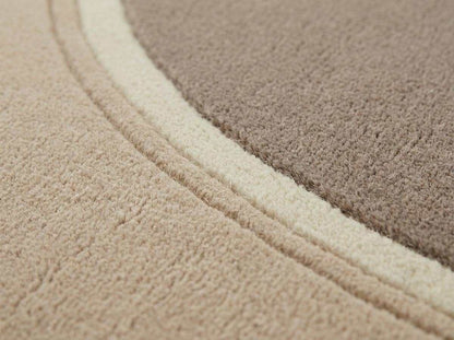 Modern neutral oval hand tufted wool area rug in beige and taupe tones in a contemporary living room setting
