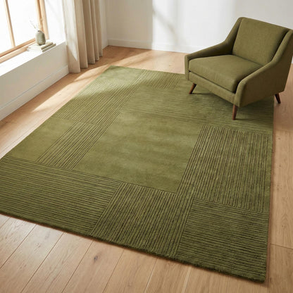 Olive green modern area rug with geometric patchwork design styled in minimalist living room with mid century chair and light wood flooring