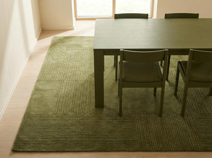 Corner detail of olive green textured area rug showing carved square pattern and clean finished edge