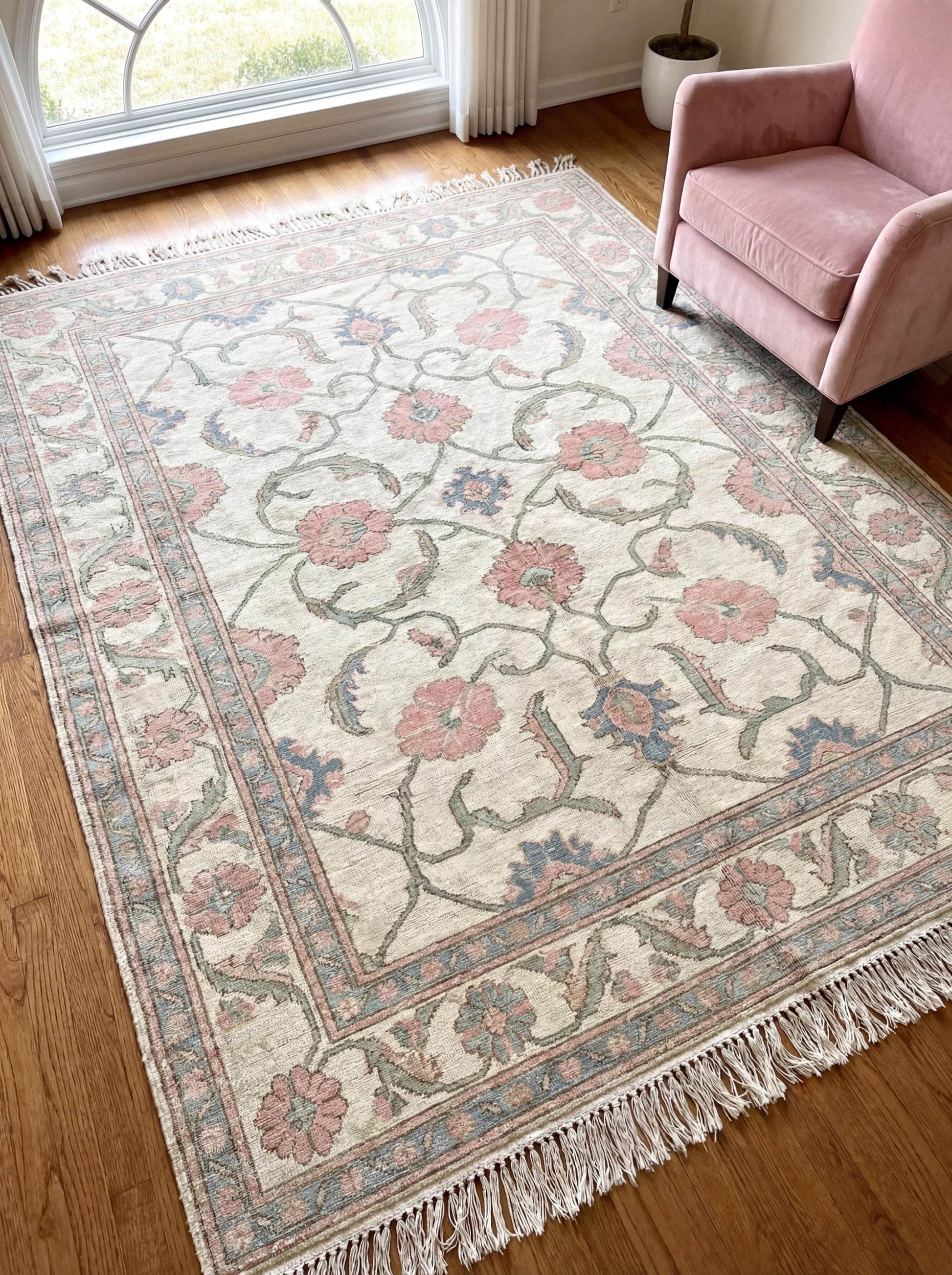 Hand knotted Oushak floral area rug in ivory with pink flowers and blue accents styled in a bright living room beside a blush armchair __etsy:7849316377