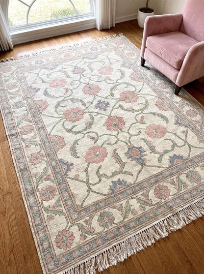 Hand knotted Oushak floral area rug in ivory with pink flowers and blue accents styled in a bright living room beside a blush armchair __etsy:7849316377