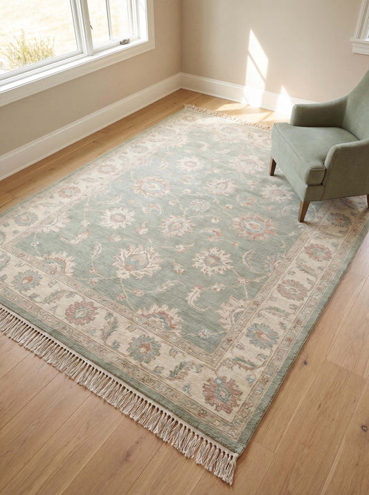 Hand knotted Oushak rug in sage green with floral pattern placed in sunlit living room with wooden floor and chair __etsy:7910096192