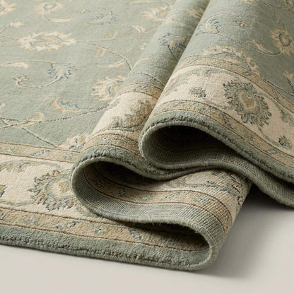 Sage green hand knotted Oushak rug with muted floral motifs and wool pile in living room setting