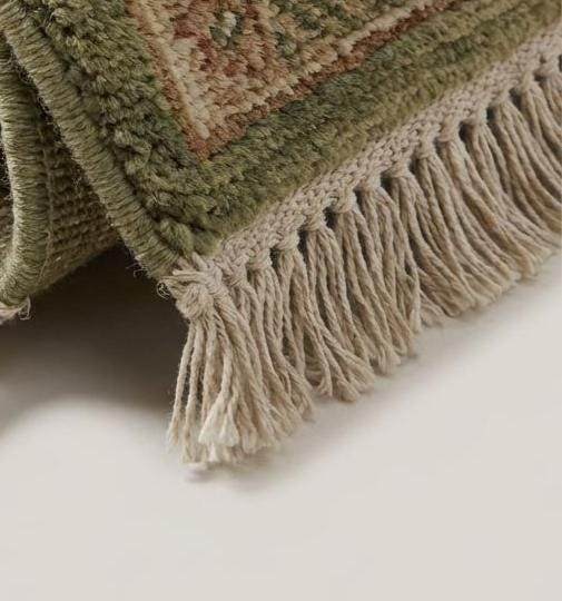 Close-up of hand knotted wool pile showing individual knots, natural wool texture, and soft sage green tones