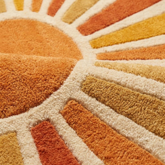 Close up texture of hand tufted wool rug showing dense plush cut pile with carved sunburst geometric pattern in rust orange and cream wool fibers