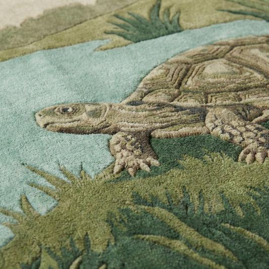Close-up of hand tufted turtle rug showing carved wool texture, raised detailing, plush pile fibers, and botanical grass design in earthy green tones.