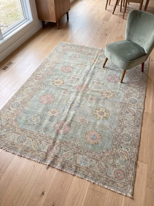 Hand knotted Oushak rug in sage green with pastel floral motifs placed in modern living room setting __etsy:7984634890