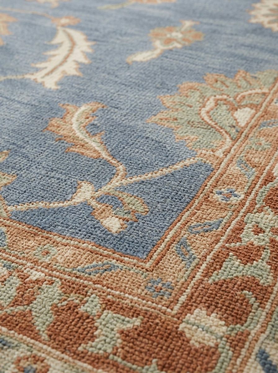Blue Oushak Rug in hand-knotted wool with a muted blue field, peach and ivory floral motifs, and patterned border