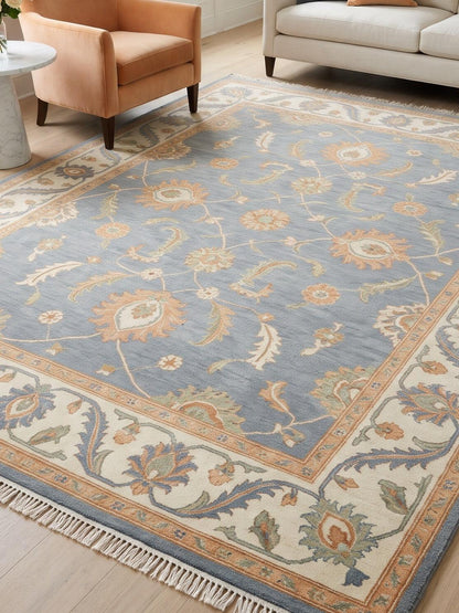 Blue Oushak Rug with a slate blue wool field, peach floral motifs, wide ivory vine border and fringe