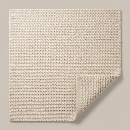 Chunky Wool Rug in ivory cream with a thick, tightly woven braided texture and a folded corner revealing its underside.