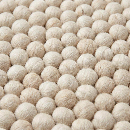 Handwoven chunky wool rug with neutral cream and beige felt balls in modern Scandinavian design