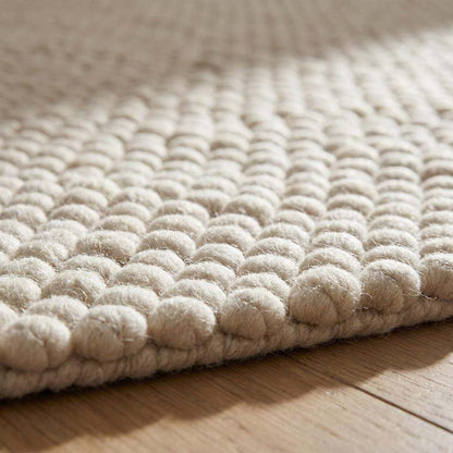 Handwoven chunky wool rug with neutral cream and beige felt balls, modern Scandinavian minimalist design for cozy living spaces