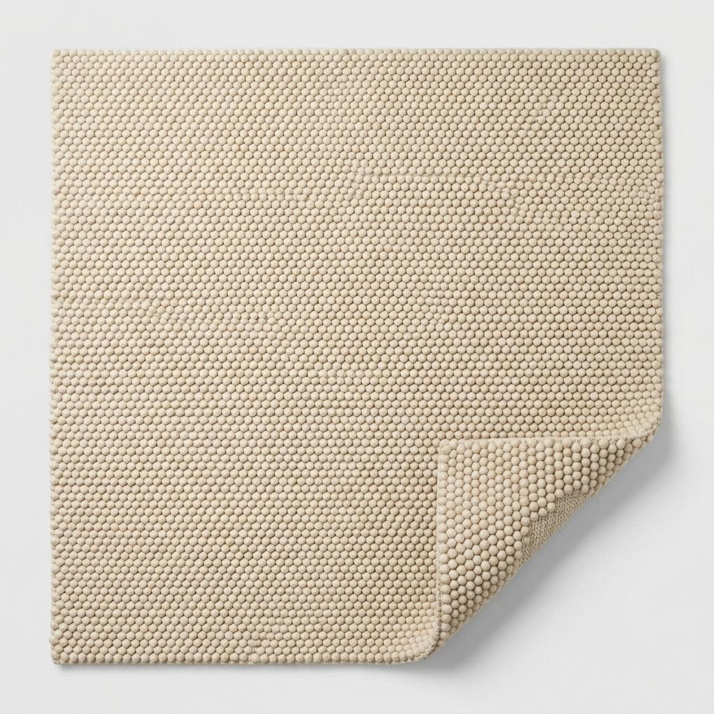Chunky Wool Rug in natural sand beige, with a dense, tightly looped woven texture and a folded corner revealing its underside.