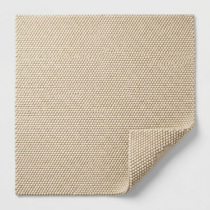 Chunky Wool Rug in natural sand beige, with a dense, tightly looped woven texture and a folded corner revealing its underside.