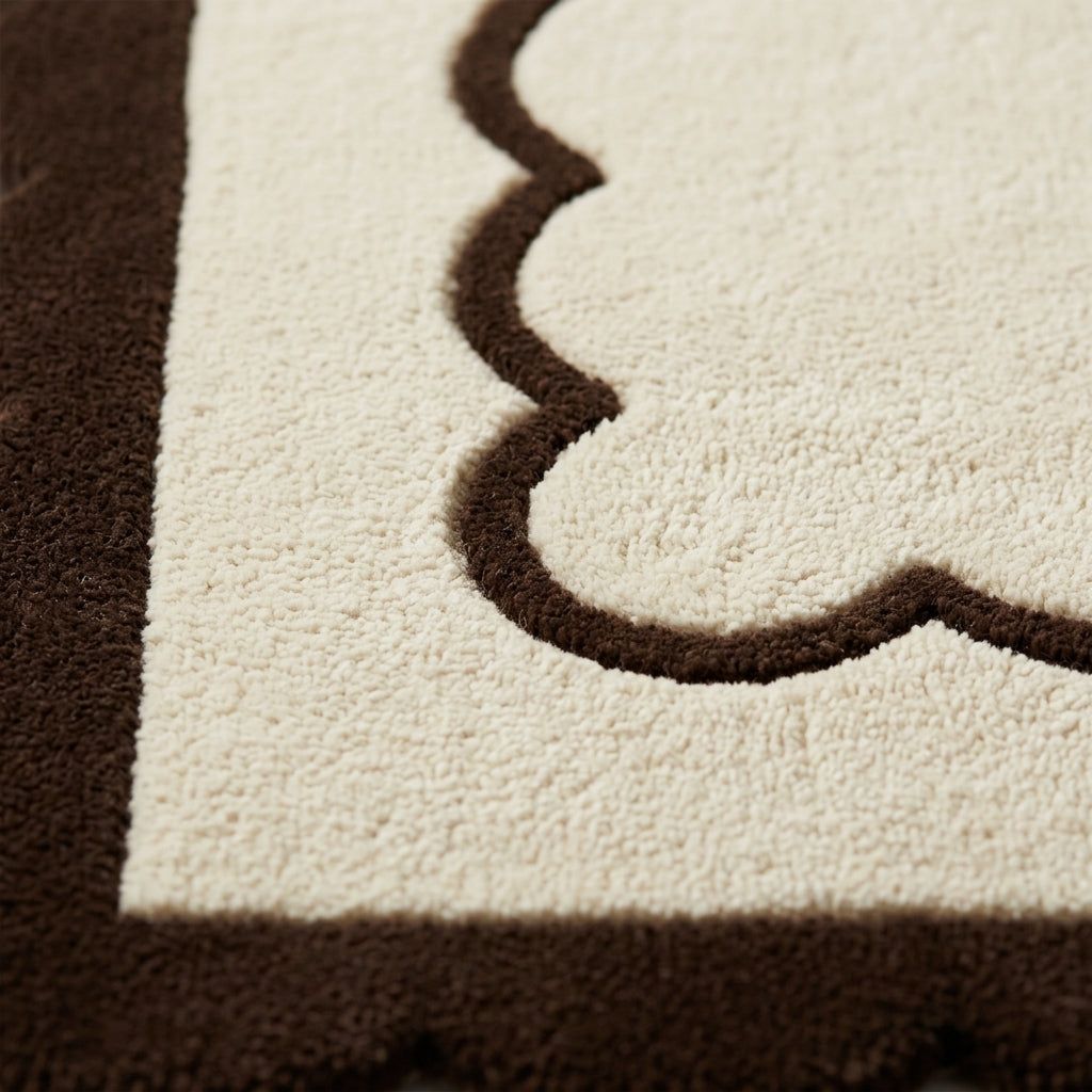 Hand-tufted wool rug in cream and chocolate brown, with a plush pile and distinctive scalloped border detail.