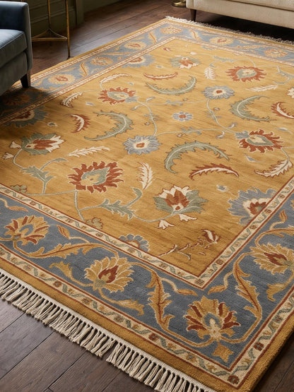 Gold Oushak Rug in golden mustard wool with rust, sage, and ivory floral motifs, slate blue border, and fringe