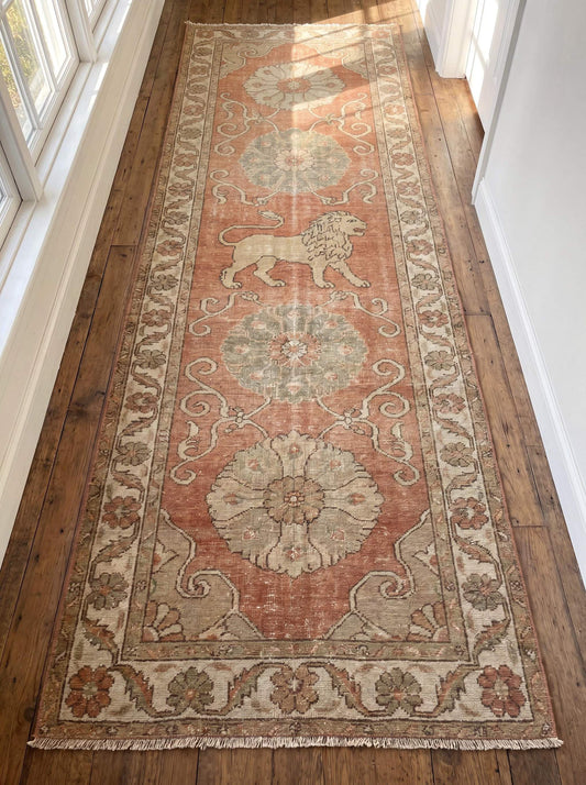 Hand knotted Oushak runner rug featuring floral medallions and lion motif in terracotta pink, ivory and sage tones displayed in a bright hallway. __etsy:8077599918