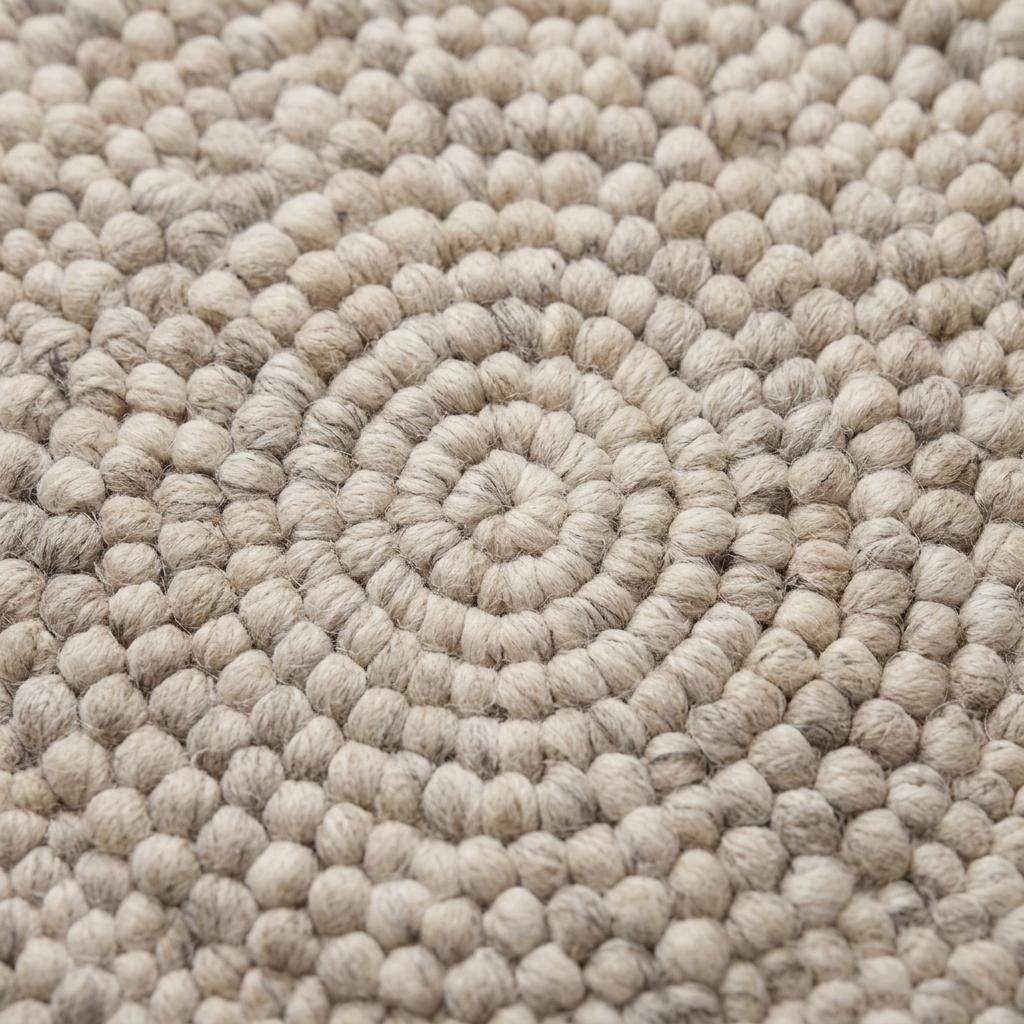 Handmade round wool felt ball rug with neutral pebble texture for Scandinavian nursery decor