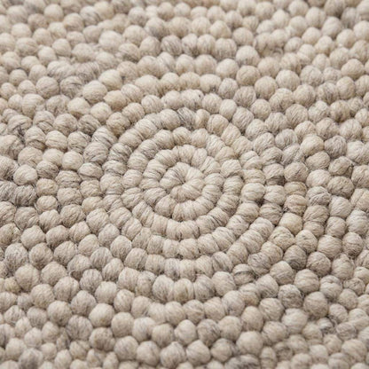 Handmade round wool felt ball rug with neutral pebble texture for Scandinavian nursery decor