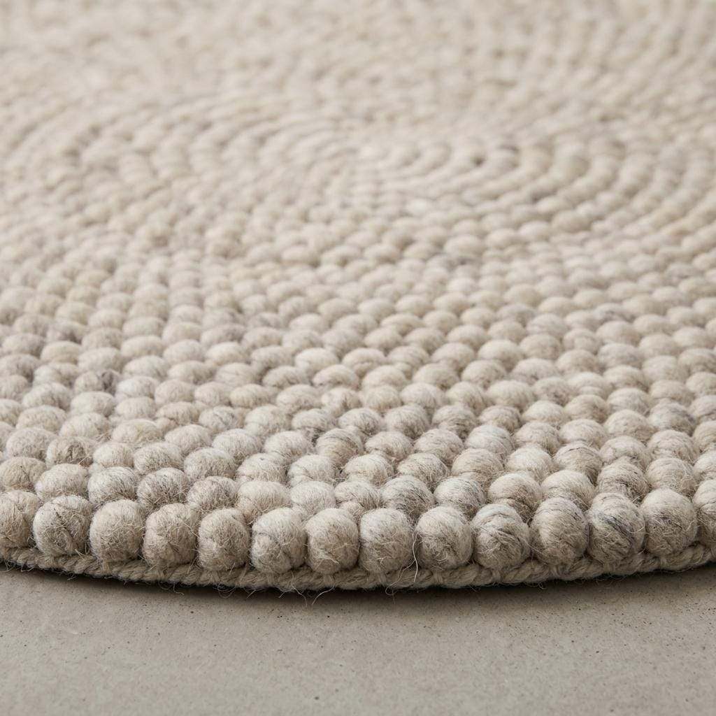 Handmade round wool felt ball rug with neutral pebble texture for Scandinavian nursery decor