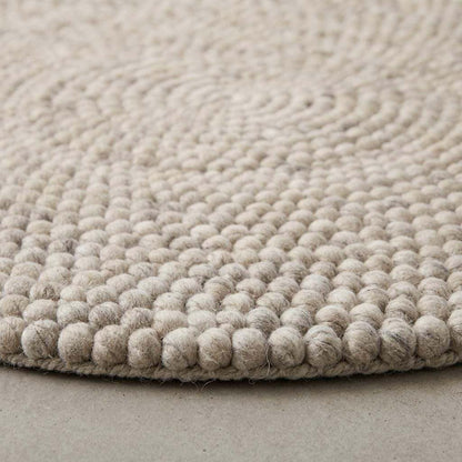 Handmade round wool felt ball rug with neutral pebble texture for Scandinavian nursery decor