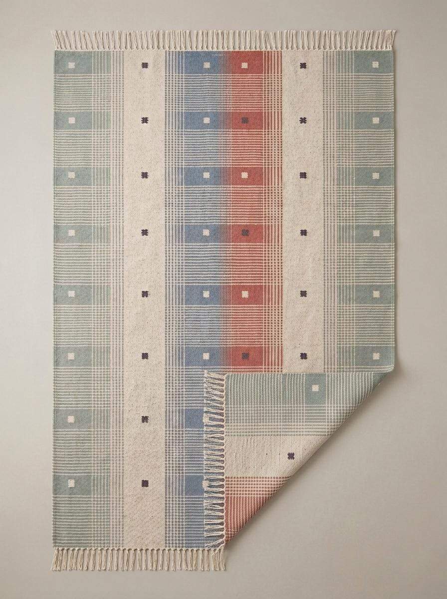 Handwoven tartan flatweave rug in sage green and terracotta with modern Scandinavian plaid design and tassel fringe