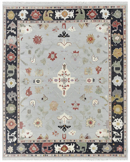 Full view of a light blue Oushak rug with a navy border and scattered multi-color floral motifs; hand-tufted.