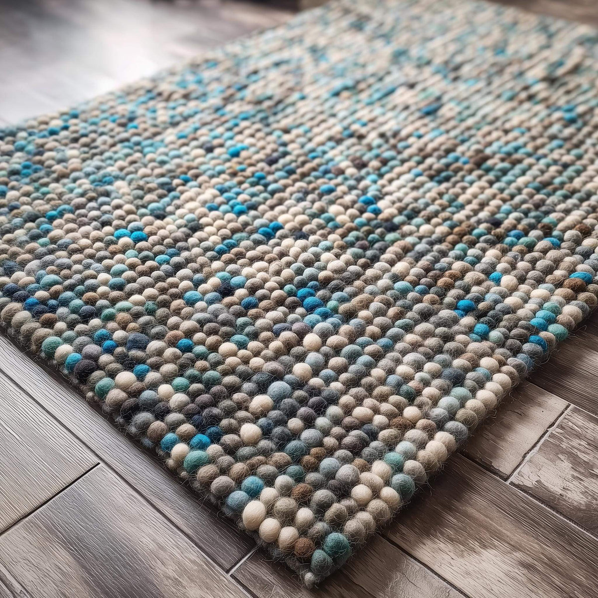 Handcrafted felt ball rug in teal, beige, and grey wool with plush pebble texture for cozy home décor
