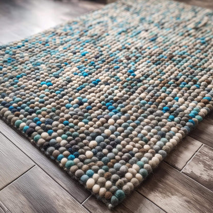 Handcrafted felt ball rug in teal, beige, and grey wool with plush pebble texture for cozy home décor