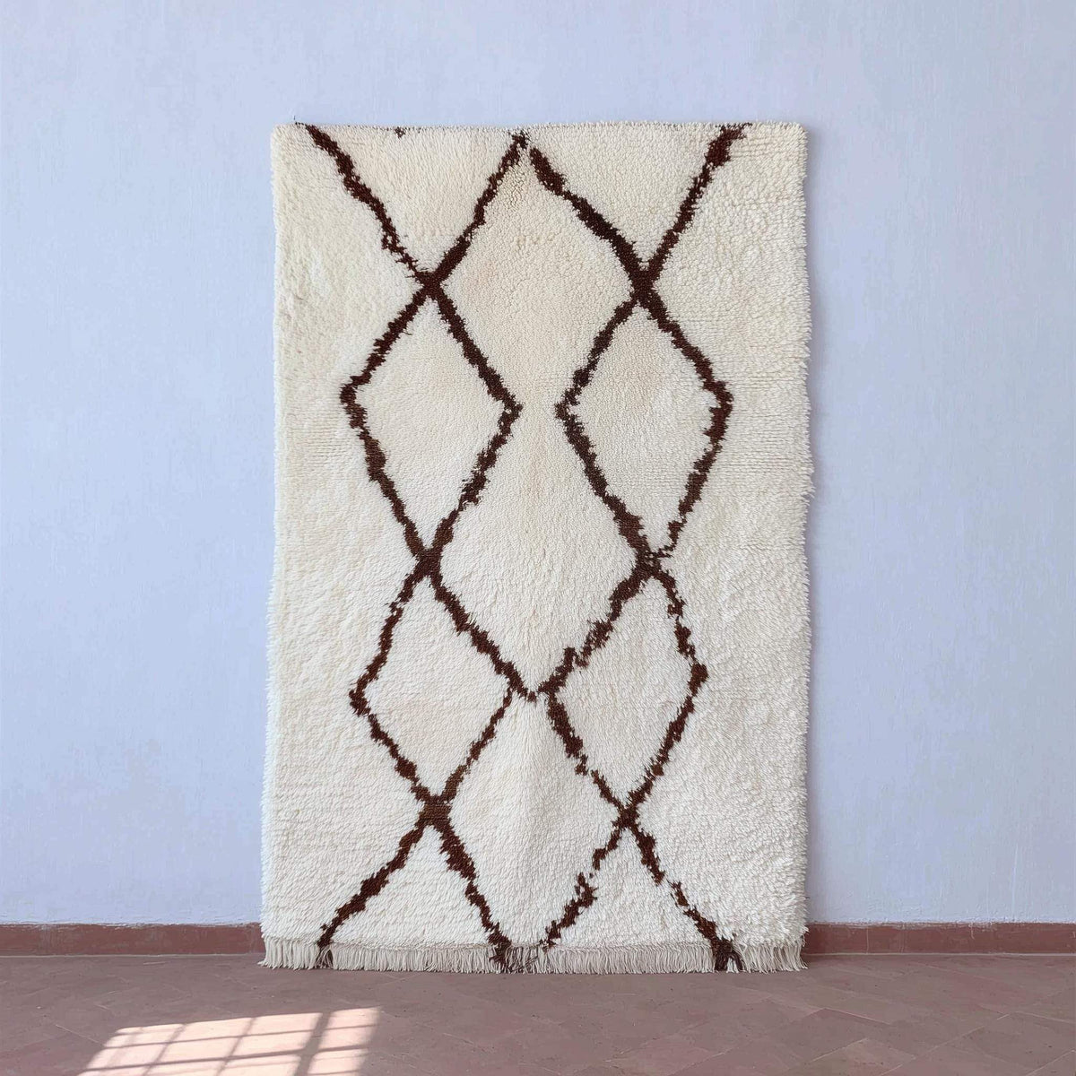 Handmade Moroccan shag rug with ivory background and dark brown diamond pattern, boho minimalist accent.