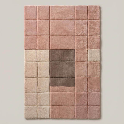Top-down view of a modern geometric area rug in blush pink, cream, and taupe tones with a plush tufted texture beside a mustard chair and wood furniture.