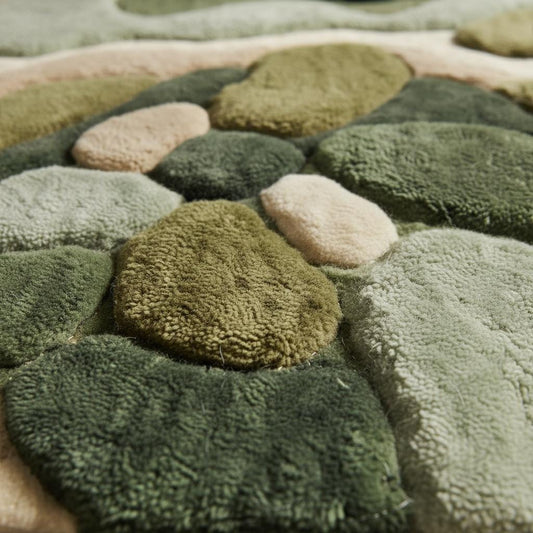 Close-up of hand tufted rug texture showing high and low pile fibers, soft plush material, and sculpted abstract pattern in green and beige tones highlighting craftsmanship and premium quality.