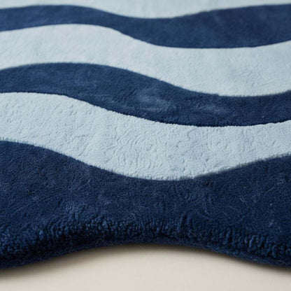 Irregular shaped curvy area rug in deep blue tones on hardwood floor, adding modern artistic style to living space.