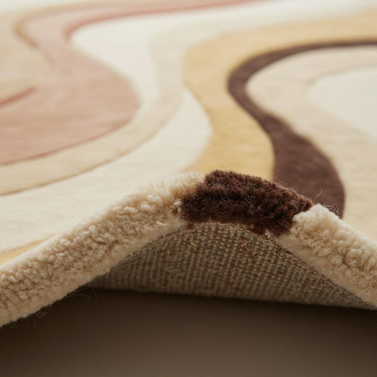 Close-up detail of abstract area rug texture showing dense plush fibers, soft pile, smooth weave, and high-quality craftsmanship in warm neutral earth tones.
