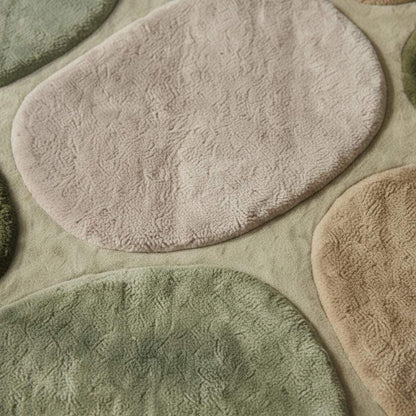 Close-up view of plush area rug texture showing thick, soft pile and sculpted pebble shapes in green and beige tones, highlighting quality craftsmanship and cozy feel.