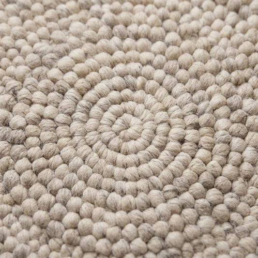 Handmade round wool felt ball rug with neutral pebble texture for Scandinavian nursery decor