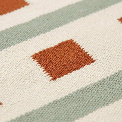 Ivory sage green flatweave dhurrie rug with terracotta square stripes and handwoven wool texture in living room setting