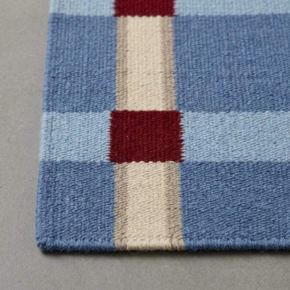 Handwoven pale blue flatweave wool rug with red grid check pattern for modern living rooms