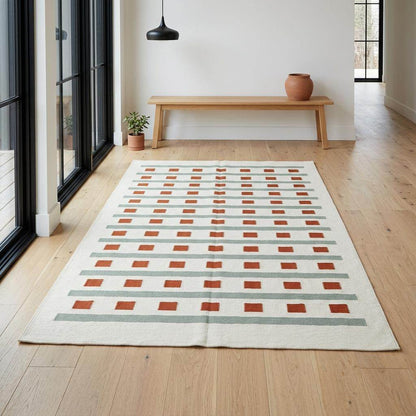 Ivory sage green flatweave dhurrie rug with terracotta stripes and squares in living room setting