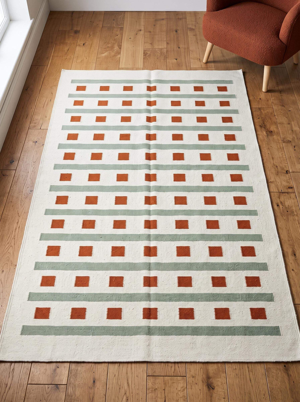 Ivory sage green flatweave dhurrie rug with terracotta square and stripe pattern in living room setting