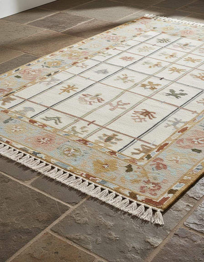 Ivory grid floral area rug with pastel border and fringe on stone floor, featuring small floral sprigs and soft muted colors