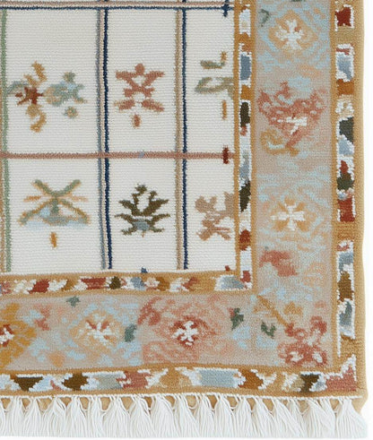 Ivory grid floral area rug with pastel floral border and fringed edges on stone floor