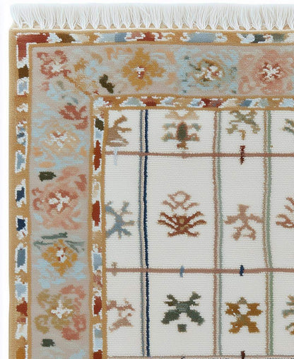 Ivory grid floral area rug with pastel border and fringed edges on stone floor