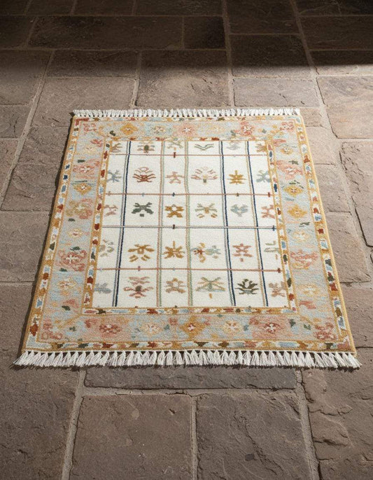 Ivory grid floral area rug with pastel border and fringe on stone floor